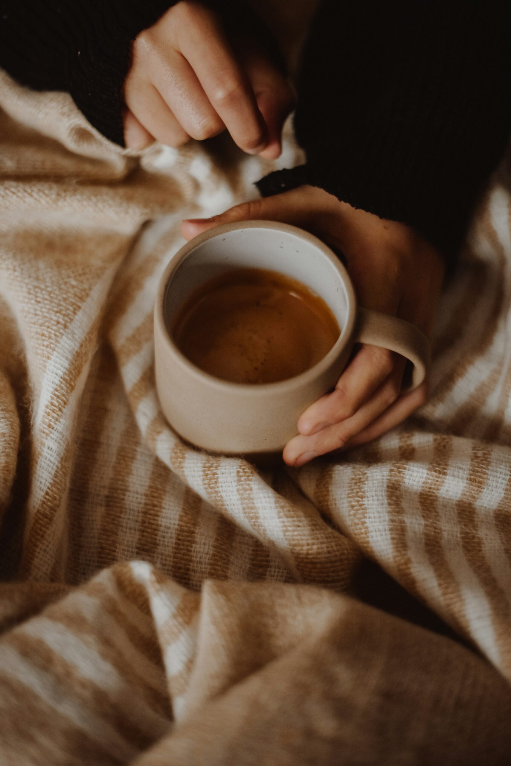 women holding a mug filled with drink whilst on a bed